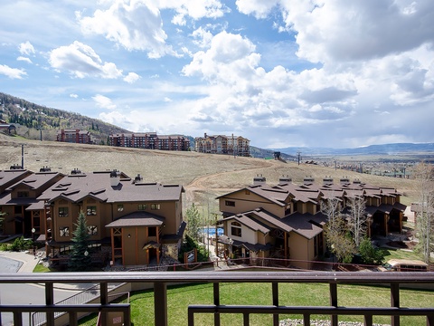 Mountain resort community featuring residential buildings positioned along scenic hillsides with dramatic alpine terrain and valley vistas stretching toward distant ranges under partly cloudy skies.