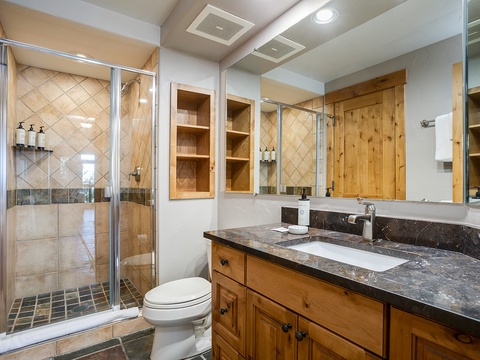 Refresh in your private spa-like bathroom featuring rustic wood cabinetry, elegant granite counters, a spacious walk-in shower, and warm natural lighting that invites relaxation.