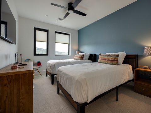 Step into your peaceful guest bedroom where two crisp beds promise restful nights. The calming blue accent wall and gentle ceiling fan create the perfect atmosphere for unwinding after your adventures.