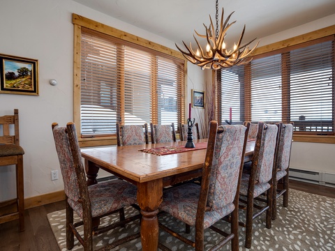 Gather around this handsome dining table beneath a striking antler chandelier, where mountain light filters through wooden blinds and memories are made over shared meals.