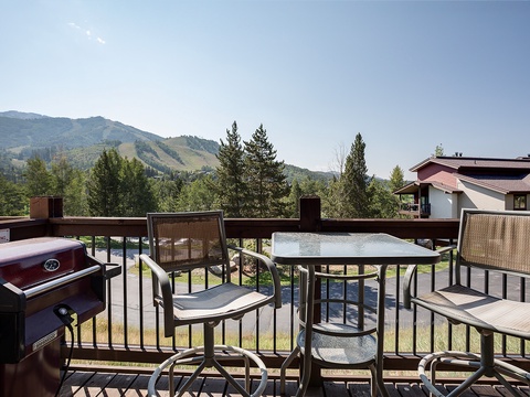Scenic mountain property featuring outdoor balcony with dining area and BBQ facilities, surrounded by natural landscape and neighboring homes.