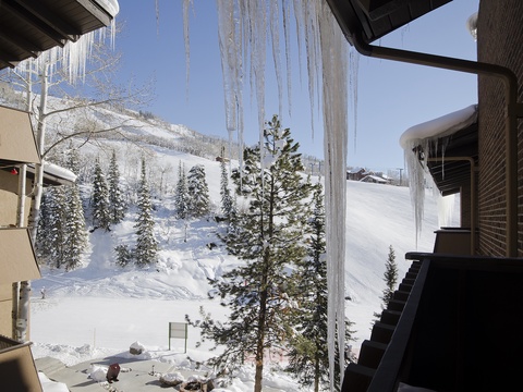 Stunning ski resort setting framed by dramatic icicles, with snow-covered slopes and frosted evergreens nestled at the base of pristine mountain peaks.