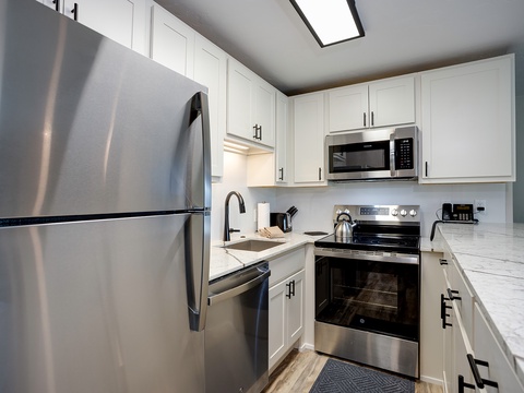 Your fully equipped modern kitchen awaits, featuring sleek stainless steel appliances, bright white cabinetry, and gleaming marble countertops perfect for preparing home-cooked meals during your stay.