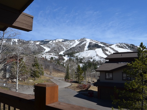 Panoramic view showcasing nearby ski slopes with clearly defined runs and snow-covered peaks, set against a bright blue sky and surrounding residential area.