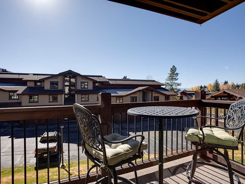 A private balcony showcases neighboring residential buildings and autumn foliage, with a small bistro table and cushioned chairs forming a quiet outdoor retreat.
