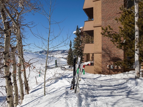 This slopeside property offers direct ski-in access, with mountain views and winter scenery framing the brick exterior. Aspen trees and evergreens line the snow-covered landscape.