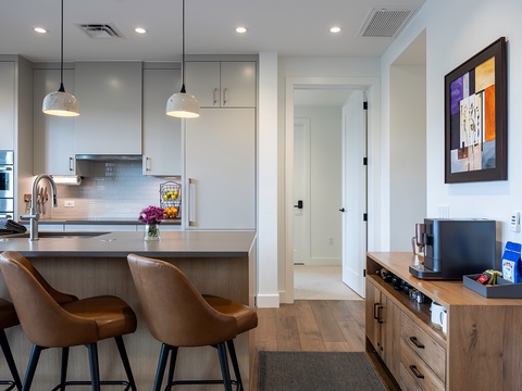 Thoughtfully designed kitchen flows seamlessly into the open living area, with modern pendant lights and sleek countertops. Warm wood tones throughout create an inviting, homey atmosphere.
