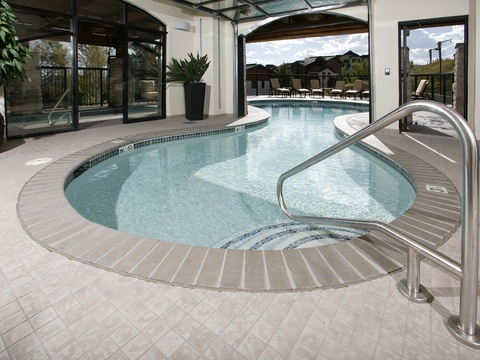 This inviting indoor-outdoor pool features a seamless flow connecting interior and exterior spaces, complete with spacious lounging areas and serene mountain views in the surrounding landscape.