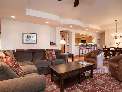 Settle into this spacious living room where plush sofas invite relaxation, warm lighting creates a cozy ambiance, and the open layout connects seamlessly to a full kitchen and elegant dining area—perfect for gathering with loved ones.