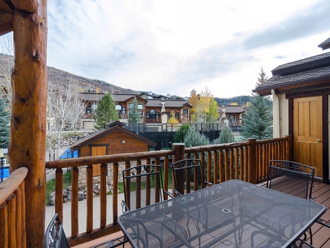 A peaceful mountain neighborhood frames this terrace, offering views of surrounding homes nestled among evergreens and autumn-touched trees, with distant slopes visible beyond.