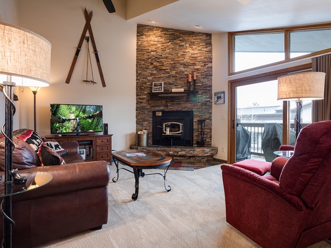 Unwind in this inviting living space with plush seating, a cozy stone fireplace, and large windows framing mountain views—your perfect retreat after a day of adventure.
