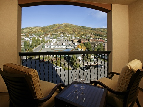 Balcony overlooking a scenic mountain landscape with colorful autumn foliage, neighboring buildings, and charming village nestled in the hillside. Comfortable seating awaits your morning coffee or evening relaxation.