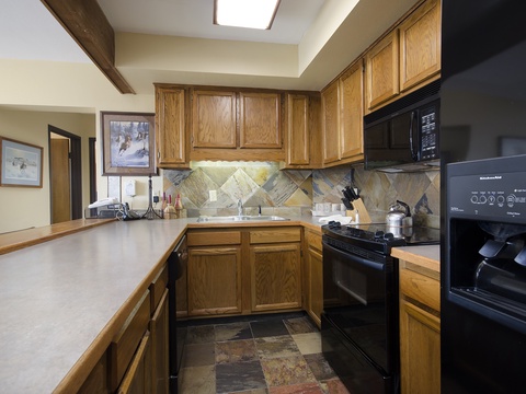 Your fully equipped kitchen features warm oak cabinetry, modern black appliances, and a decorative stone-tile backsplash—perfect for preparing homemade meals during your mountain getaway.
