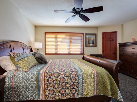 Sink into this cozy bedroom, where the rich wooden furniture and vibrant quilt create a warm, welcoming retreat. The gentle ceiling fan keeps you comfortable while natural light filters softly through the blinds.