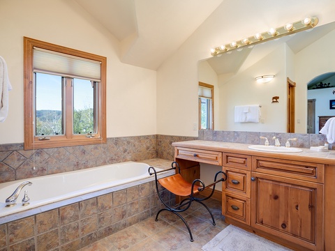 Unwind in your spa-like bathroom with a luxurious soaking tub framed by warm wood accents and natural light, offering peaceful views to help you relax after a day of adventure.