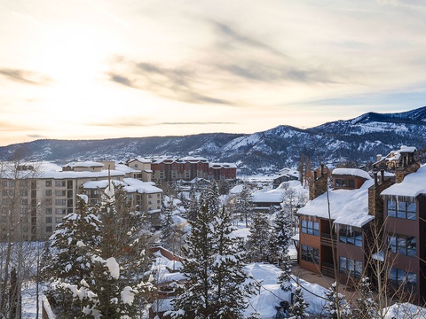 A picturesque winter mountain resort nestled among snow-draped evergreens and distant peaks, offering a serene alpine setting for your seasonal getaway.