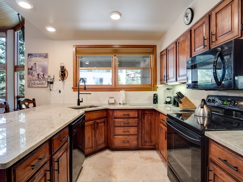 Your fully equipped kitchen features rich wood cabinetry, granite counters, and modern black appliances—perfect for preparing hearty mountain meals after a day exploring Steamboat Springs.