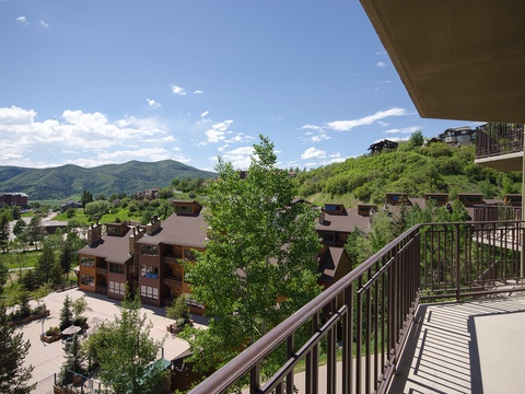 A scenic mountain resort community spreads across rolling green hillsides beneath distant peaks and blue skies, offering a peaceful retreat setting.