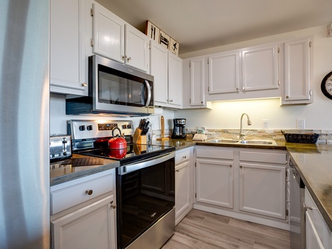 A fully equipped kitchen awaits with granite countertops, white cabinetry, and modern appliances, perfect for preparing your favorite meals during your stay.
