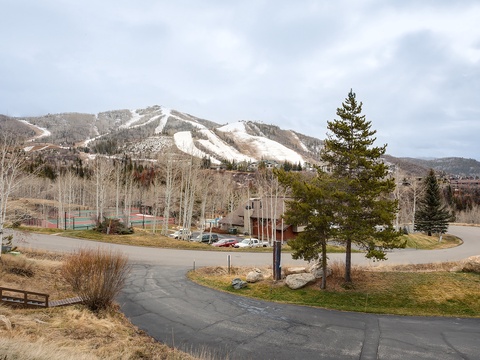 Property nestled at the base of snow-capped ski slopes, surrounded by evergreen forests and open mountain terrain with nearby recreational facilities.