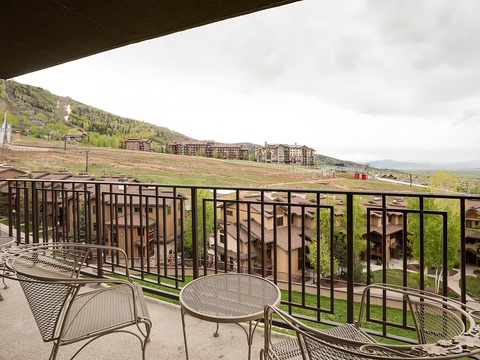 Mountain resort balcony with seating and scenic views of slopes, neighboring properties, and distant peaks under overcast skies.