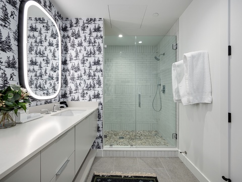 Step into your spa-like sanctuary with a glass-enclosed shower, whimsical wallpaper, and modern touches designed for your ultimate relaxation.