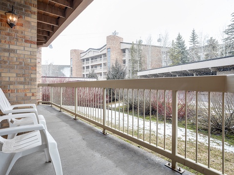 Private balcony with seating overlooking a winter landscape of snow-dusted grounds, evergreens, and mountain resort buildings in the crisp alpine air.