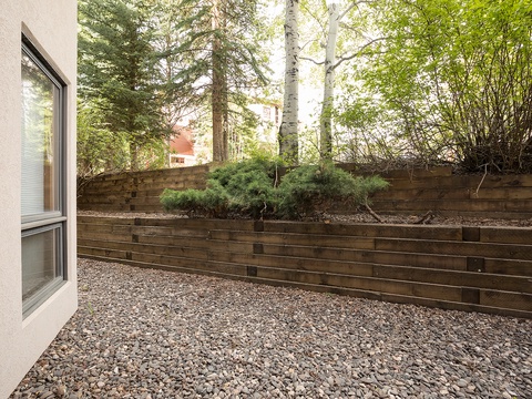 A serene private patio enclosed by natural wood fencing, featuring mature trees and greenery that create a peaceful outdoor retreat adjacent to your ground-level unit.