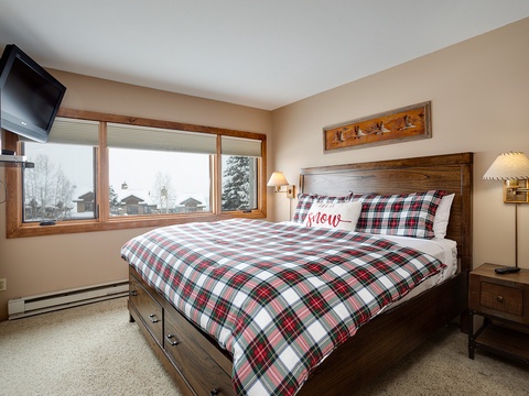 Drift off in your cozy bedroom with mountain views, warm plaid bedding, and thoughtful touches like bedside reading lamps and a wall-mounted TV for relaxed evenings.