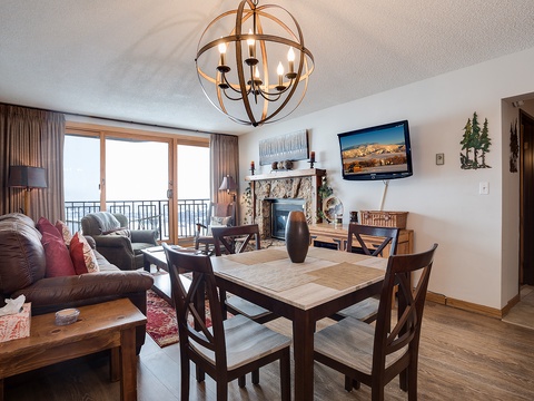 Your open-concept living space blends comfort with mountain charm—gather around the dining table, relax by the stone fireplace, or step out onto your balcony to enjoy breathtaking views.
