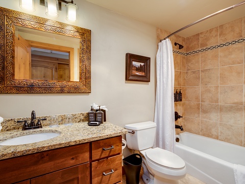 Your private bathroom features a granite vanity, warm wood cabinetry, and a spacious tub-shower combo with elegant tile surround—perfect for unwinding after a day of adventure.
