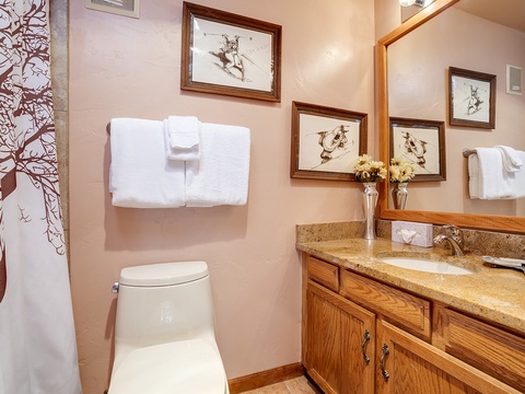 Your private bathroom features warm wood cabinetry, granite countertops, and thoughtful mountain-inspired artwork. Fresh towels and essential toiletries await your arrival.