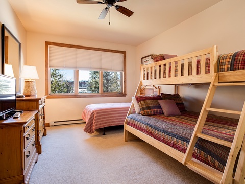 Your cozy bedroom features comfortable bunk beds with warm quilts, a TV for entertainment, and large windows framing beautiful tree views—perfect for restful nights.
