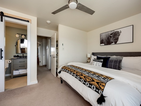 Settle in and unwind in this modern bedroom with crisp linens, a rustic barn door to your private bathroom, and a ceiling fan to keep you cool.