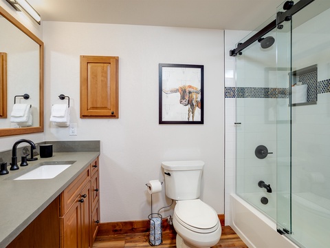 Your private bathroom features a glass-enclosed tub-shower combo, modern fixtures, and warm wood accents that create a welcoming space to refresh after your adventures.