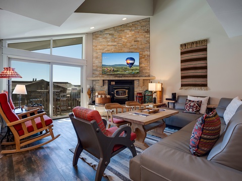 Unwind in your open-concept living room, where natural light floods through floor-to-ceiling windows framing mountain views, while the stone fireplace and stylish furnishings create the perfect retreat after a day of adventure.
