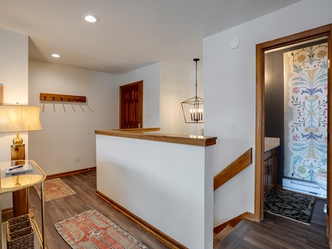 A bright, welcoming hallway leads to a charming bathroom adorned with artistic floral wall decor, while warm wood accents and a cozy lamp-lit corner create a homey atmosphere throughout your stay.