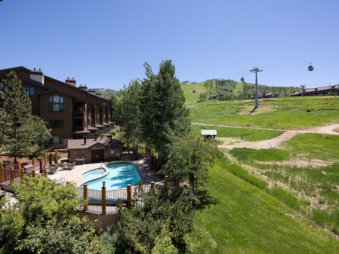 Ski resort property nestled at the base of rolling slopes with gondola access, pool, and expansive mountain views. Lush summer greenery surrounds multi-level lodgings ideal for year-round adventure.