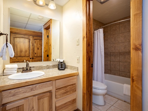 Your private bathroom features warm wood accents and modern convenience. Fresh towels await on the counter, while the tub-shower combo with its tiled surround offers a refreshing retreat after your adventures.