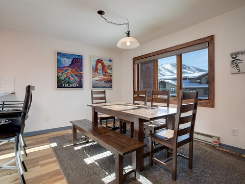 Gather around this inviting dining table where sunlight spills across warm wood floors. The mountain views through the window create a stunning backdrop for your morning coffee and shared meals.