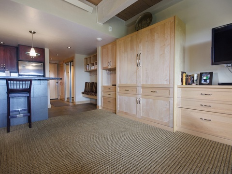 This open studio features warm wood cabinetry, built-in storage, a kitchenette with bar seating, and modern comforts including a flat-screen TV—everything you need for a relaxed mountain getaway.