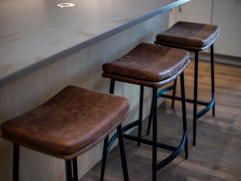 A modern bar counter with three sleek stools invites you to gather for casual meals or morning coffee. The rich leather seats and clean lines create a perfect spot for conversation.