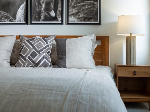 Sink into plush linens and let the warmth of mid-century modern design envelop you. This thoughtfully styled bedroom invites restful nights with its earthy wood tones, layered textures, and artistic touches.