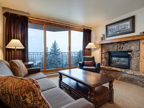Settle into your mountain retreat with a stone fireplace and floor-to-ceiling windows framing stunning alpine views. Cozy up on plush sofas as natural light fills this welcoming living room.