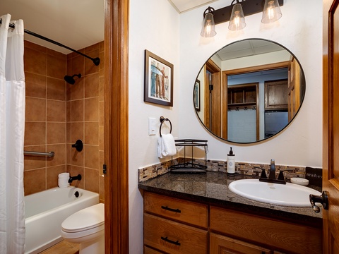 Step into your beautifully appointed bathroom featuring a granite vanity, round mirror with modern lighting, and a relaxing tub-shower combo with warm tile accents. Fresh towels and thoughtful details await you.