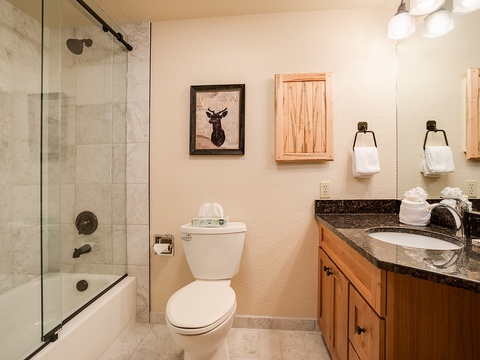 Your spacious bathroom features elegant granite counters, a glass-enclosed tub/shower combo, and warm natural wood cabinetry—perfect for unwinding after a mountain adventure.