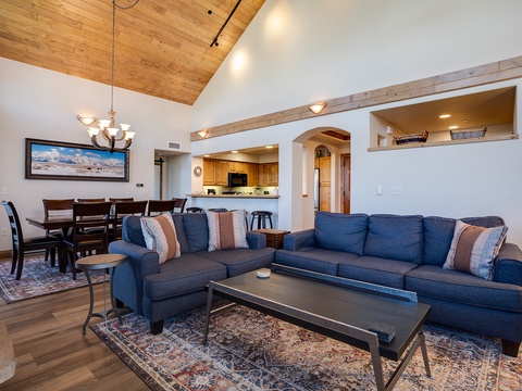 Unwind in this beautifully designed living space featuring a spacious sofa, cozy dining area, and fully equipped kitchen—all beneath stunning vaulted ceilings with warm wood accents that create your perfect mountain retreat.
