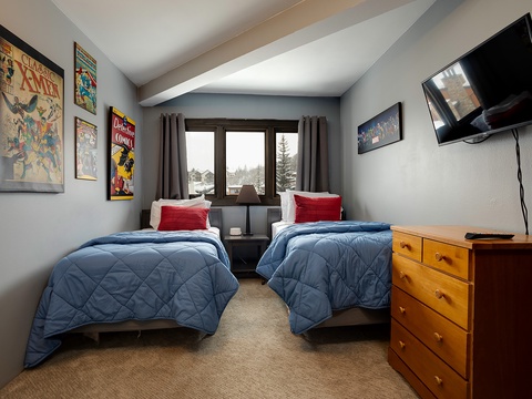 Your cozy retreat features two plush beds with soft blue comforters, inviting you to unwind after a day of adventure. Enjoy your favorite shows on the wall-mounted TV, surrounded by fun comic-themed art.