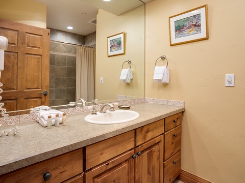 Your private bathroom features warm wood cabinetry, fresh white linens, and a spacious tiled walk-in shower—perfect for refreshing after a day exploring the area.