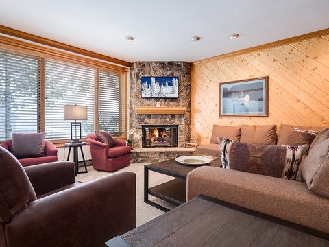 Sink into plush seating by your crackling stone fireplace, with warm pine walls and mountain light streaming in—your cozy alpine retreat awaits.